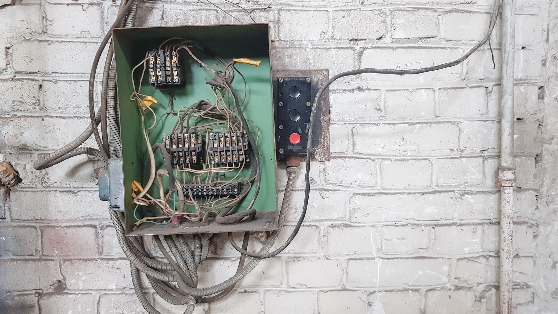 Old electrical panel on the wall of the house. Electric cables stick out from the electric panel on the white brick wall of the old house